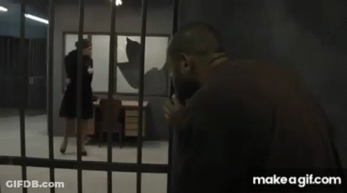 A Woman In A Black Dress Is Walking Through A Jail Cell . GIF