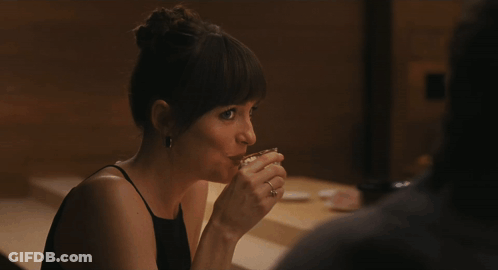 A Woman In A Black Dress Sits At A Table GIF