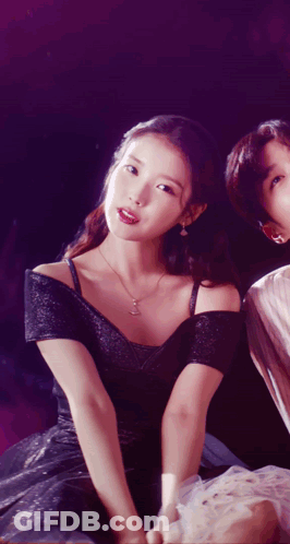 A Woman In A Black Dress Sitting Next To A Man In A White Shirt GIF