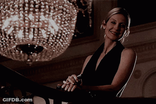 A Woman In A Black Dress Smiles While Sitting On A Staircase GIF