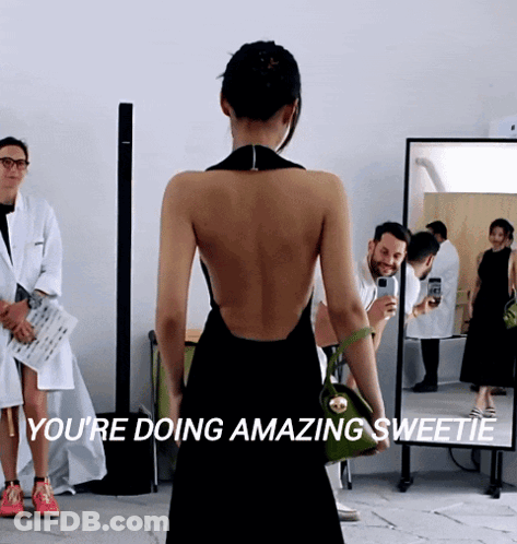 A Woman In A Black Dress Stands In Front Of A Mirror With The Words " You 'Re Doing Amazing Sweetie " GIF