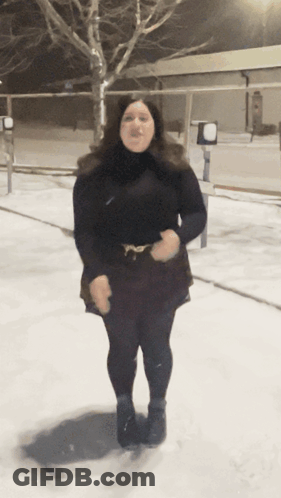 A Woman In A Black Dress Stands In The Snow GIF
