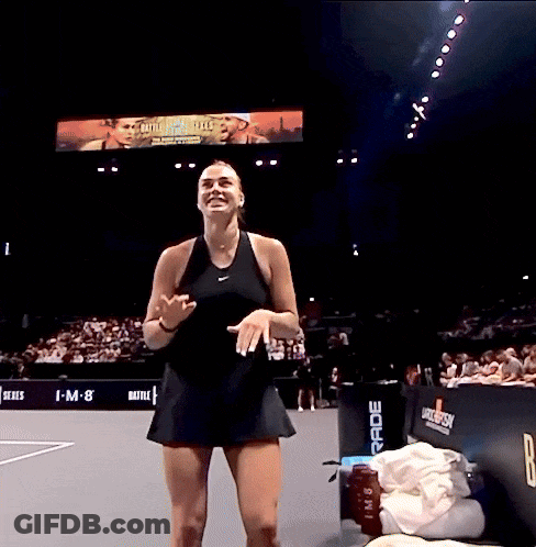 A Woman In A Black Dress Stands On A Tennis Court In Front Of A Large Screen That Says I-M-8 GIF
