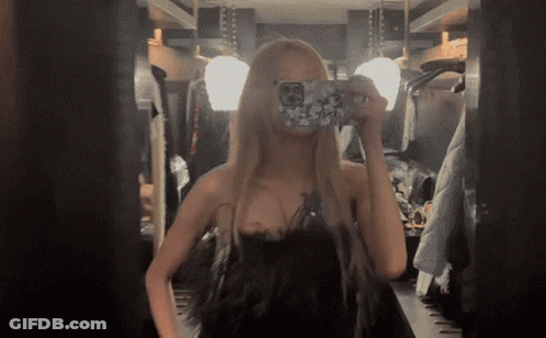 A Woman In A Black Dress Takes A Picture Of Herself In A Mirror GIF