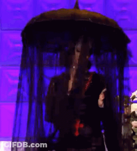 A Woman In A Black Dress With A Cross Around Her Neck Is Holding An Umbrella . GIF