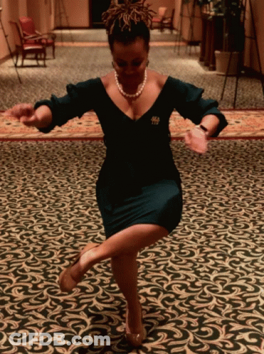 A Woman In A Black Dress With A Pearl Necklace And A Brooch With The Letter T On It Is Dancing On A Rug GIF