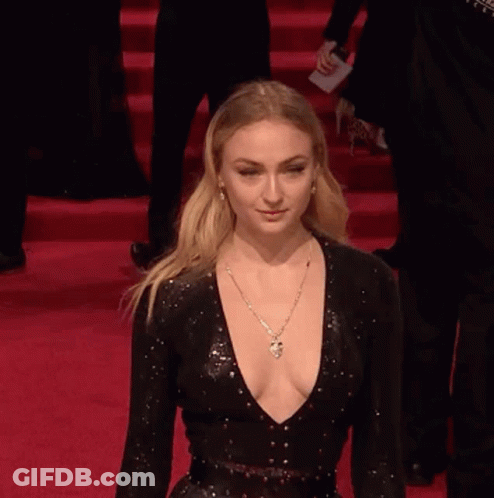 A Woman In A Black Dress With A Plunging Neckline Is Walking Down A Red Carpet . GIF