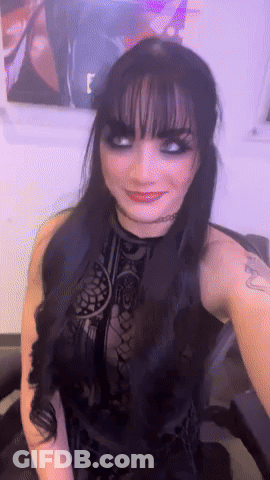A Woman In A Black Dress With A Tattoo On Her Arm Is Smiling GIF
