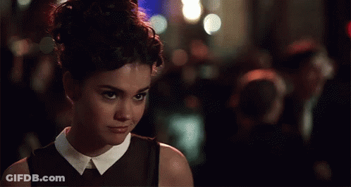 A Woman In A Black Dress With A White Collar Looks At The Camera GIF