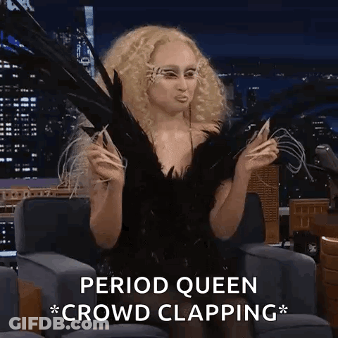 A Woman In A Black Dress With Feathers On Her Face Is Sitting In A Chair With The Words Period Queen Crowd Clapping . GIF
