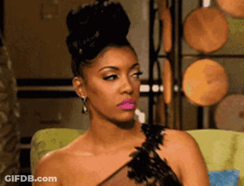 A Woman In A Black Dress With Pink Lipstick Is Sitting On A Chair . GIF