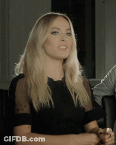 A Woman In A Black Dress With Sheer Sleeves GIF