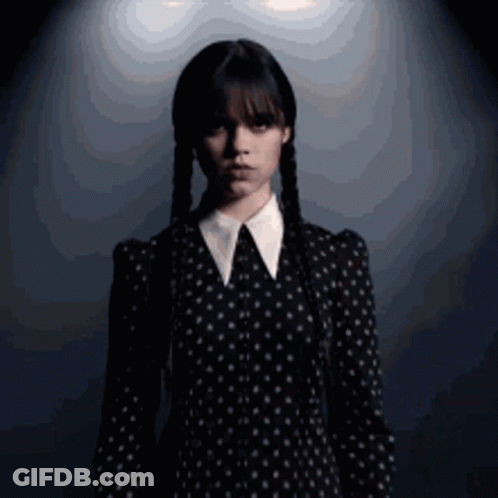 A Woman In A Black Dress With White Polka Dots And Braids GIF