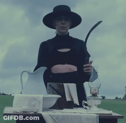 A Woman In A Black Hat Holds A Sickle In Her Hand GIF
