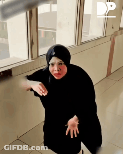 A Woman In A Black Hijab Is Standing In Front Of A Window With The Letter D On The Bottom Right GIF