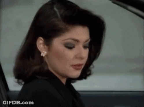 A Woman In A Black Jacket And Earrings Is Sitting In A Car Looking Out The Window . GIF
