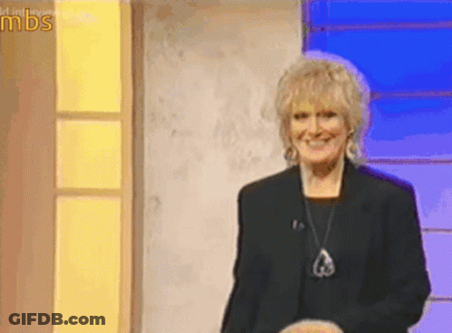 A Woman In A Black Jacket And Necklace Is Smiling On A Stage In Front Of A Sign That Says Mds GIF