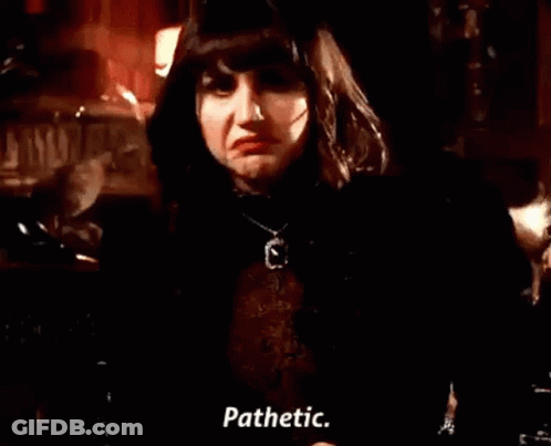 A Woman In A Black Jacket And Necklace Is Standing In A Dark Room And Talking . GIF
