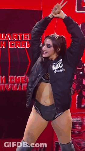 A Woman In A Black Jacket And Shorts Is Dancing In Front Of A Sign That Says Quarterback Crew . GIF