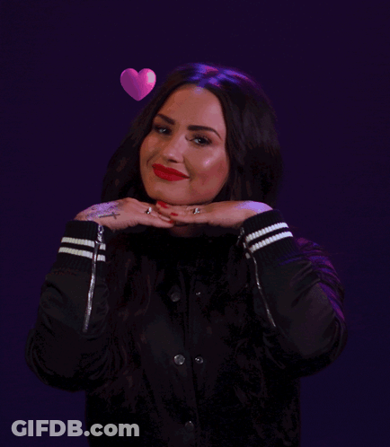 A Woman In A Black Jacket Has Hearts Floating Around Her Head GIF
