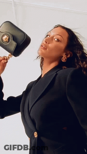 A Woman In A Black Jacket Is Holding A Black Purse On Her Shoulder GIF