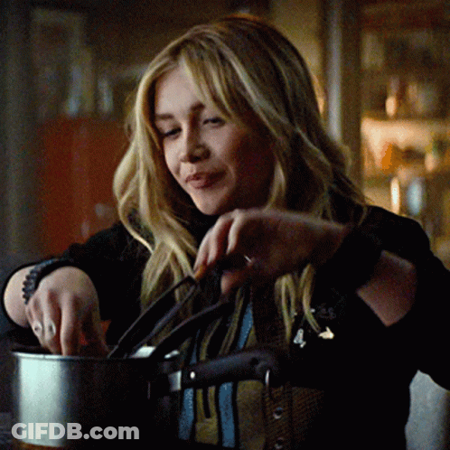 A Woman In A Black Jacket Is Holding A Pot And Smiling GIF