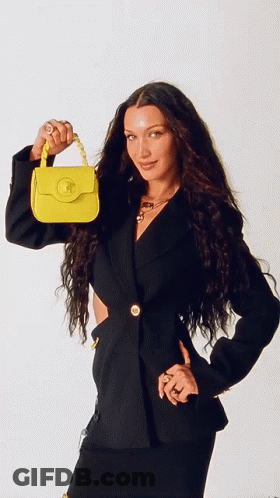 A Woman In A Black Jacket Is Holding A Small Yellow Bag GIF