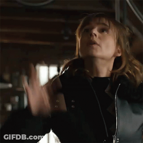 A Woman In A Black Jacket Is Holding Her Hands Up In The Air GIF