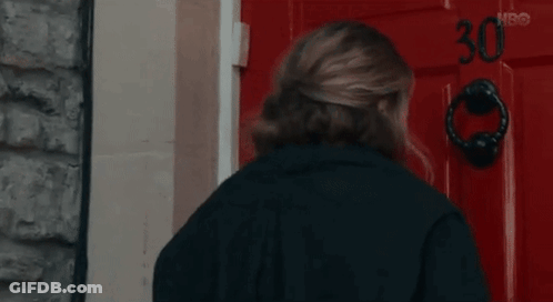 A Woman In A Black Jacket Is Knocking On A Red Door . GIF