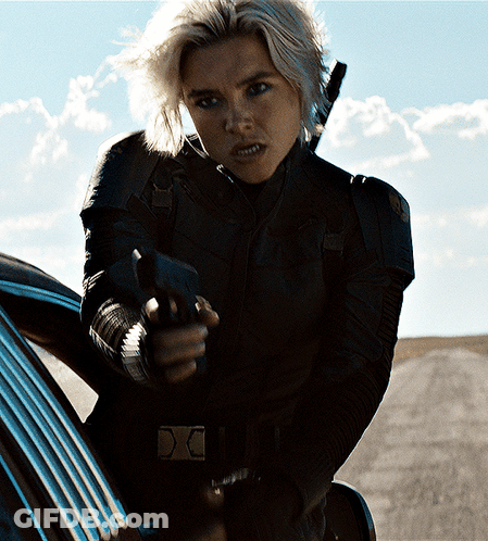 A Woman In A Black Jacket Is Pointing A Gun At Someone GIF