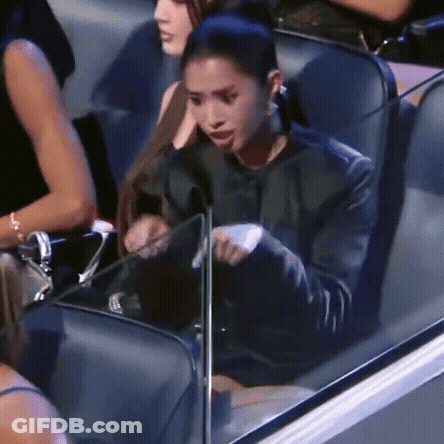 A Woman In A Black Jacket Is Sitting In A Stadium Holding A Piece Of Paper . GIF