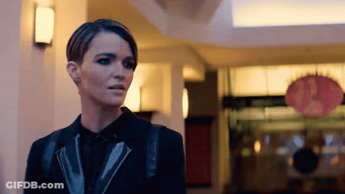 A Woman In A Black Jacket Is Standing In A Building GIF