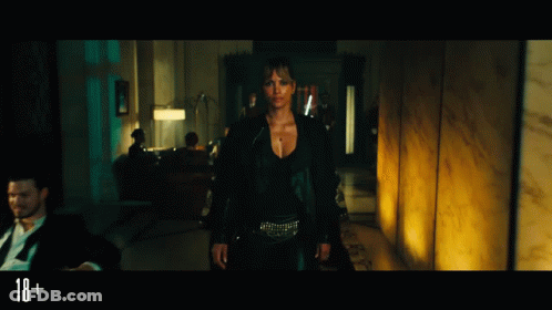 A Woman In A Black Jacket Is Standing In A Dark Room With A Sign That Says 18+ In The Corner GIF