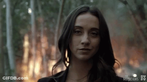 A Woman In A Black Jacket Is Standing In Front Of A Fire In The Woods . GIF