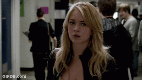 A Woman In A Black Jacket Stands In A Hallway Looking At The Camera GIF