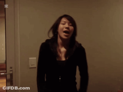 A Woman In A Black Jacket Stands In Front Of A Wall With An X In The Corner GIF