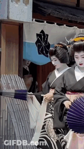 A Woman In A Black Kimono Is Holding A Fan In Front Of A Blue And White Flag With A Cross On It GIF