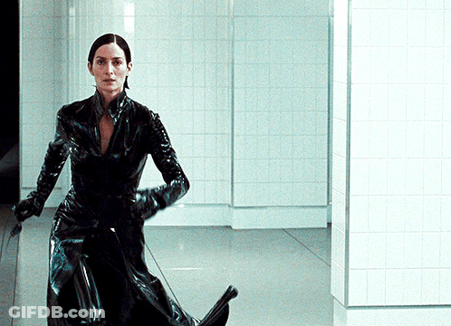 A Woman In A Black Latex Suit Is Standing In A Hallway GIF