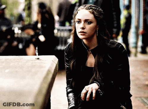 A Woman In A Black Leather Jacket Is Sitting On A Sidewalk Looking At Something . GIF