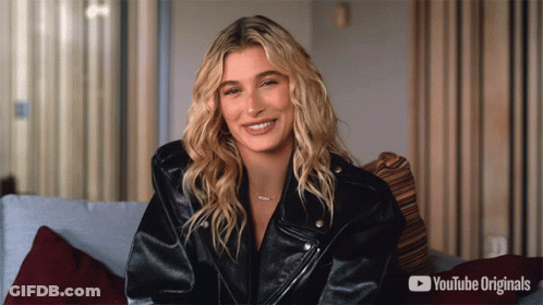 A Woman In A Black Leather Jacket Is Smiling In Front Of A Youtube Originals Advertisement GIF