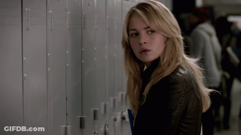 A Woman In A Black Leather Jacket Is Standing In Front Of A Row Of Lockers GIF