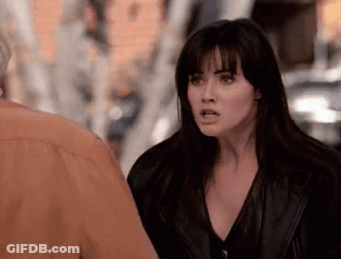 A Woman In A Black Leather Jacket Is Standing Next To A Man In An Orange Shirt . GIF