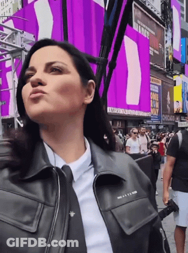 A Woman In A Black Leather Jacket Stands In Front Of A Chicago Sign GIF