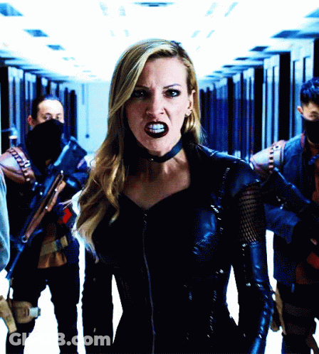 A Woman In A Black Leather Outfit Stands In A Hallway GIF