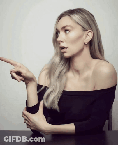 A Woman In A Black Off The Shoulder Top Points Her Finger At Something GIF