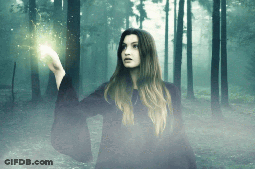A Woman In A Black Robe Is Holding A Light In Her Hand In A Forest GIF