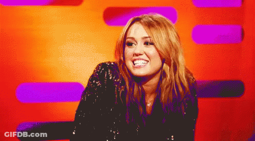 A Woman In A Black Sequined Top Smiles In Front Of A Purple And Orange Background GIF
