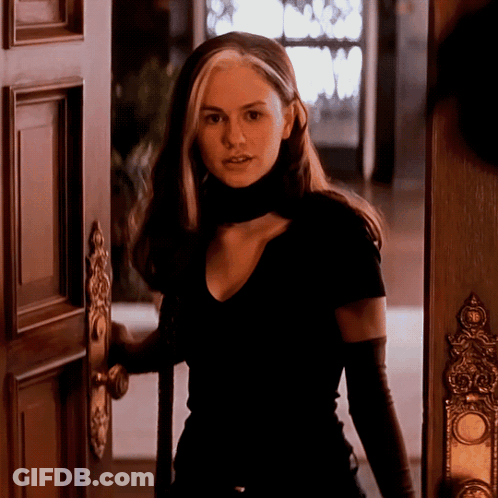 A Woman In A Black Shirt And Black Gloves Stands In A Doorway GIF