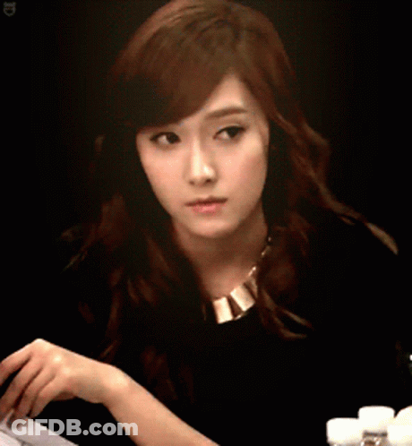 A Woman In A Black Shirt And Gold Necklace Looks At Something GIF