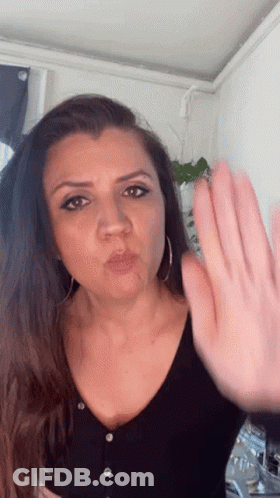 A Woman In A Black Shirt Is Blowing A Kiss And Making A Stop Sign With Her Hand GIF